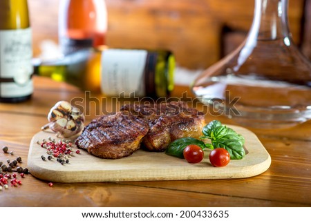 A big pork steak with spices, tomatoes and bottles of wine on the background