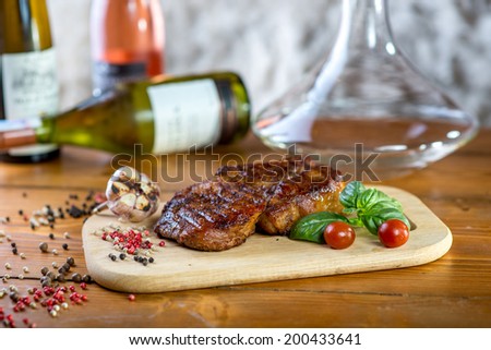 A big pork steak with spices, tomatoes and bottles of wine on the background