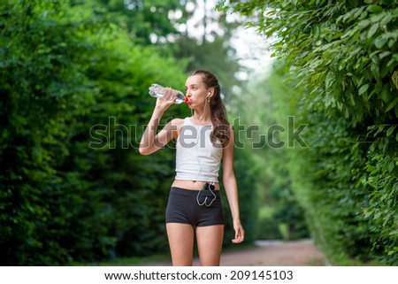 Woman athlete takes a break. Drinking water, out on a run in the park