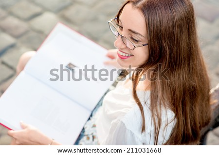 Young beautiful woman reading red book in the city