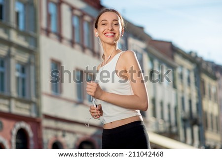 Running woman jogging to music in the city. Runner wearing earphones and armband for smart phone. Female fitness jogger training outside for healthy lifestyle.