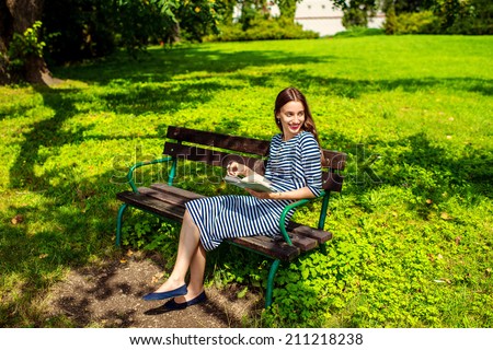Young woman reading book on the bench smiling and happy. Pretty young woman enjoying spring in the park.