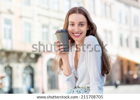 A businesswoman with cup of coffee to go against sunny city landscape