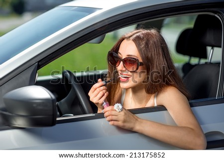An attractive young woman applying lipstick in the rear view mirror while driving
