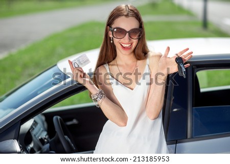 Young woman showing a key and license in front of the car. Girl pass successfully driving exam.