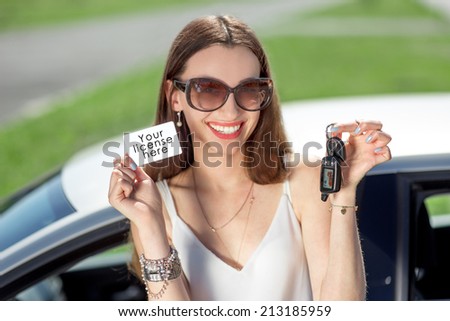 Young woman showing a key and license in front of the car. Girl pass successfully driving exam.