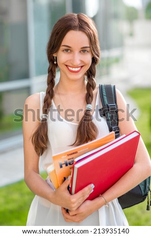 Student girl outdoors with backpack and books going to school and smiling