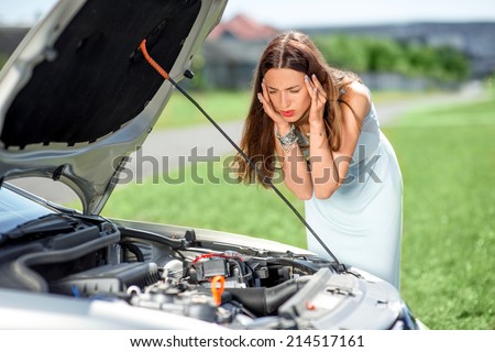 A woman waits for assistance near her car broken down on the road side.
