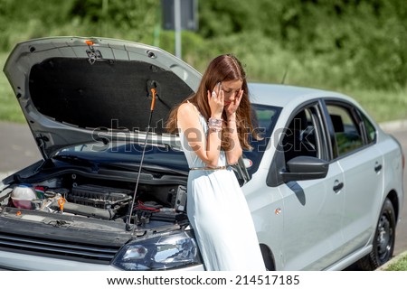 A woman waits for assistance near her car broken down on the road side.