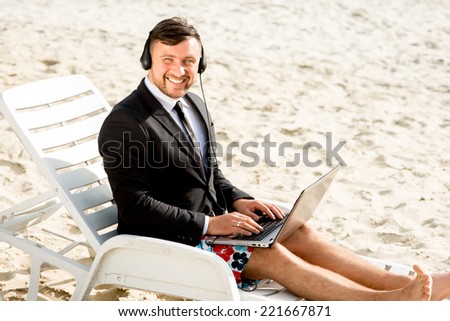 Businessman dressed in suit and shorts having video call with laptop on the sunbed at the beach