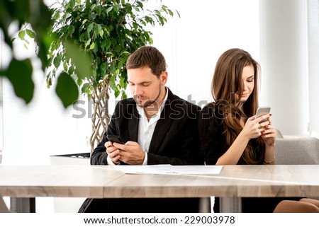 Young couple being busy using their smart phones at the restaurant turned away from each other.