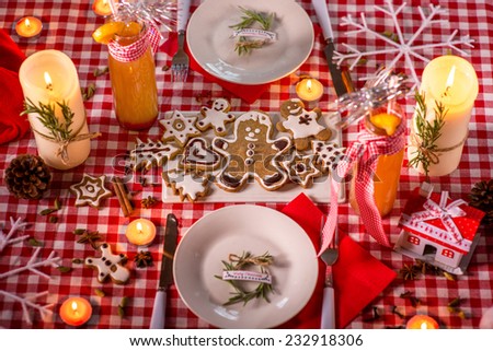 Sweet Christmas decorated table with candles, cookies, drinks and lights on background on red checkered tablecloth