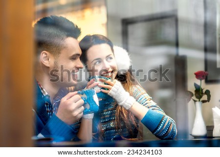 Young loving couple dressed in blue sweater sitting with knitted coffee cups at the cafe in winter