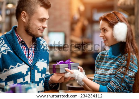 Man making proposal giving a gift box to his girlfriend dressed in blue sweaters in the cafe