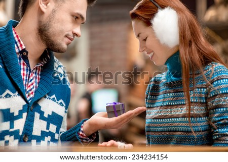 Man making proposal giving a gift box to his girlfriend dressed in blue sweaters in the cafe