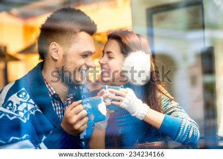 Young loving couple dressed in blue sweater sitting with knitted coffee cups at the cafe in winter
