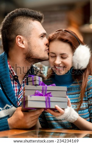 Young couple dressed in blue knitted sweaters with gift boxes at the cafe in winter