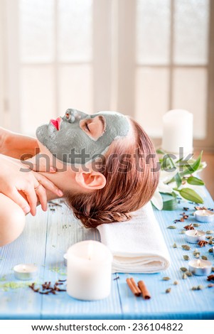 Young woman with spa facial mask on her face lying on blue table with flower, candles and sea salt in the beaty salon. Side view