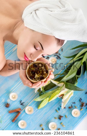 Smiling young woman with cup of herbal tea in bath towel in spa salon. Herbal treatment.