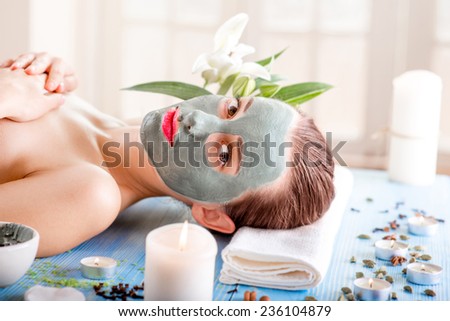 Young woman with spa facial mask on her face lying on blue table with flower, candles and sea salt in the beaty salon. Side view