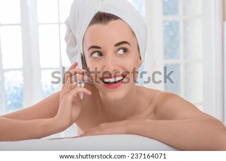 Young smiling and naked woman with towel on her head speaking phone in the bathroom or spa salon