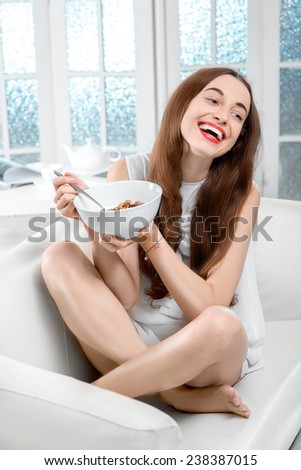 Young positive woman eating granola breakfast on the couch at home
