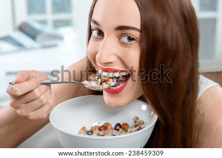 Young positive woman eating granola breakfast on the couch at home. Close-up