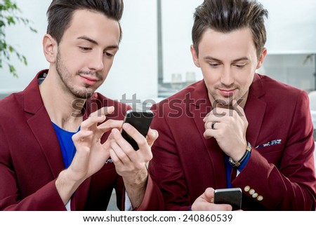 Two brothers twins in red jackets using smart phones at the office