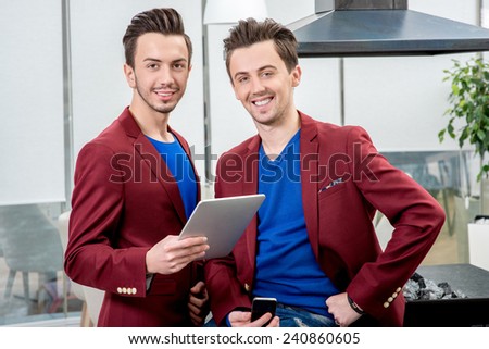 Two brothers twins restaurateurs in red jackets working with tablet at the restaurant. Family business