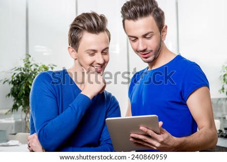 Friendly brothers twins in blue sweaters using digital tablet in the white home interior.