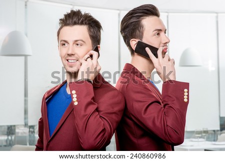 Friendly business brothers twins in red jackets using mobile phone in white office