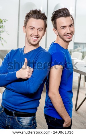 Friendly brothers twins in blue sweaters embracing in the white home or restaurant interior. Family relationship between two brothers