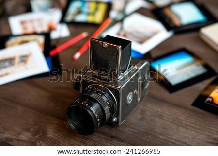 Old full frame film camera on the table with printed photos and pencils