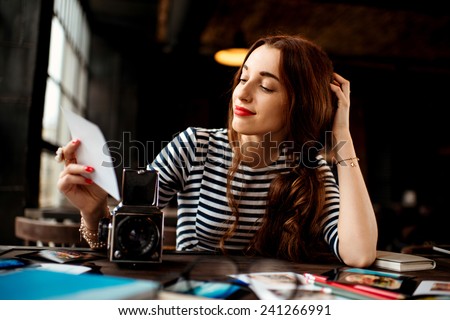 Young woman photographer looking at the printed photos with old 6x6 frame camera sitting in the cafe with loft design interior