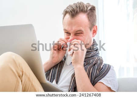 Ill man suffering from rhinitis sitting on the couch with laptop at home