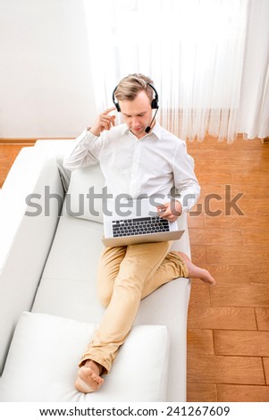 Man having video call with laptop and headphones sitting on the couch at home