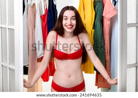 Smiling woman opening the doors of wardrobe dressed in red underwear