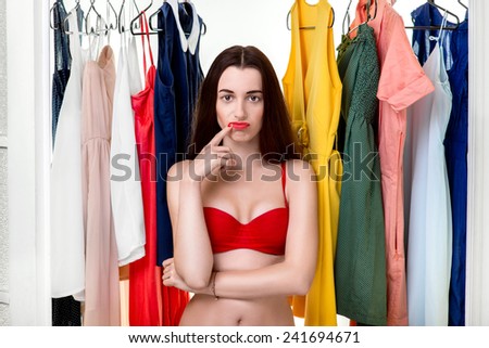 Young woman in underwear thinking what dress to wear in front of the clothes in wardrobe. Nothing to wear concept