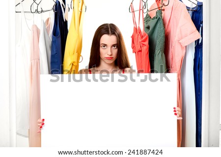 Young woman holding empty white board in the wardrobe. Nothing to wear concept