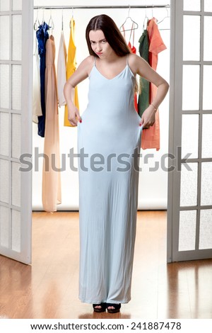 Young happy woman trying on new dress to wear in front of the wardrobe