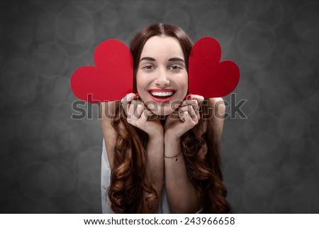Happy and joyful young woman holding red hearts on grey background in studio. Happy valentines greeting concept