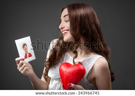 Woman falling in love holds heart and boyfriend photo in studio