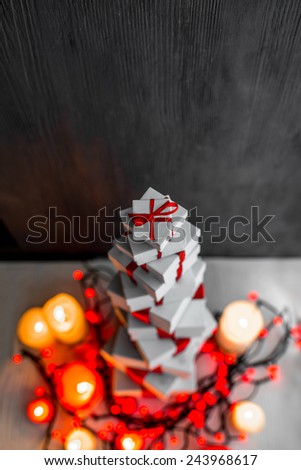 A pile of gift boxes with red ribbons on wooden background with candles and space for text. Greeting card concept