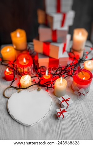 A pile of gift boxes with red ribbons on wooden background with candles and space for text. Greeting card concept