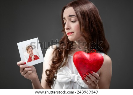 Upset woman holding photo card with boyfriend and broken heart. Failed relationship concept