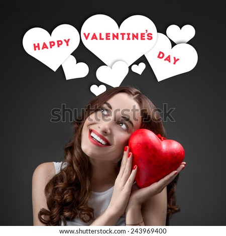 Happy and joyful young woman holding red heart on grey background with graphic hearts. Happy valentines greeting concept