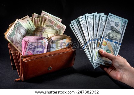 Pile of Ukrainian money in the wallet and american dollars in the hand on black background