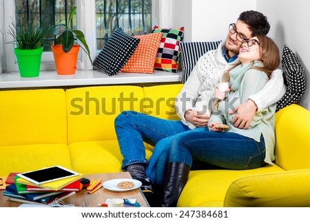 Young couple in sweaters and eyeglasses sitting with coffee on the couch at home