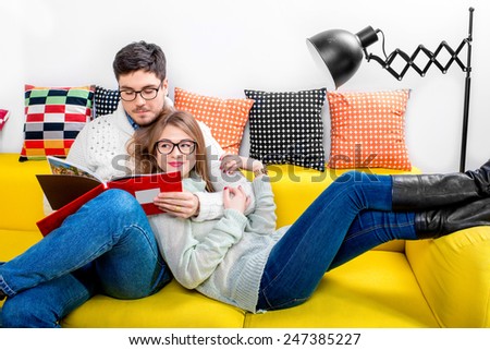 Young couple in sweater and eueglasses reading books on the couch at home