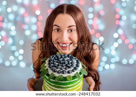 Beautiful girl holding happy birthday cake and smiling looking at camera on festive light background